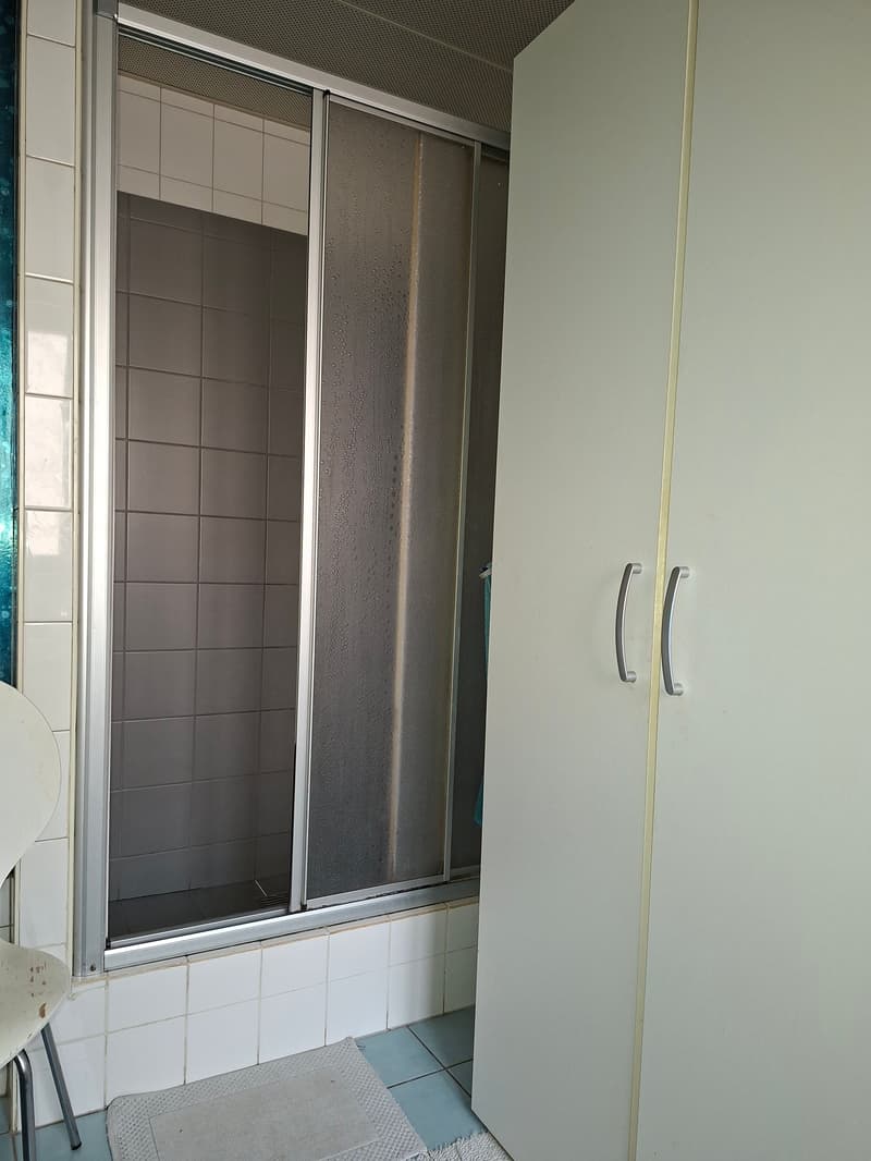 Bathroom with a sliding glass shower, white tiles, white shelf, chair