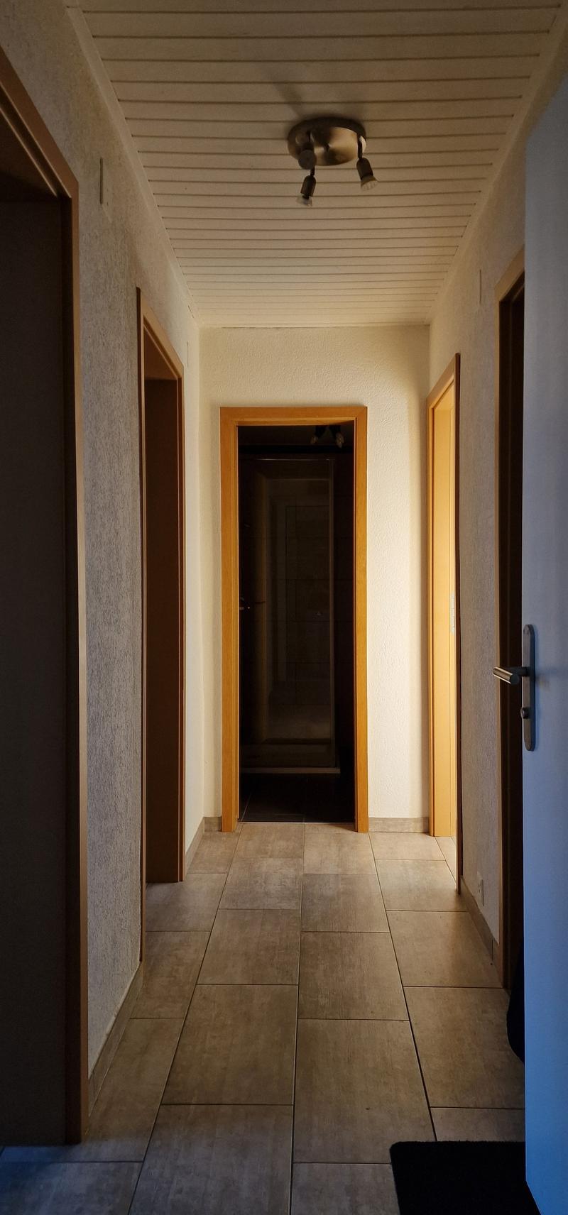 Empty hallway with tiled floor, wooden doors, and a ceiling light fixture.