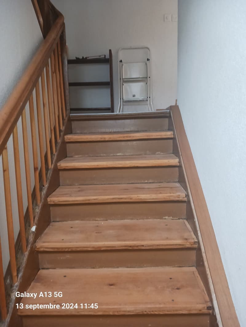 wooden staircase with wooden handrail, wooden steps, white walls, small shelf with items, folding ladder