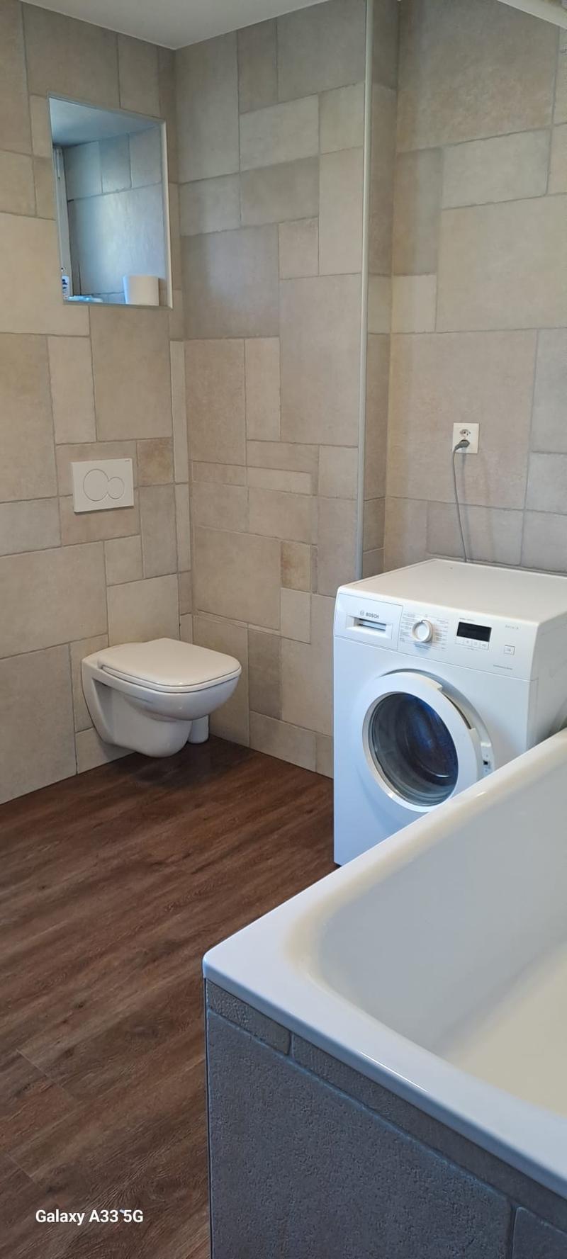Bathroom with toilet, washing machine, bathtub, tiled walls, wooden floor