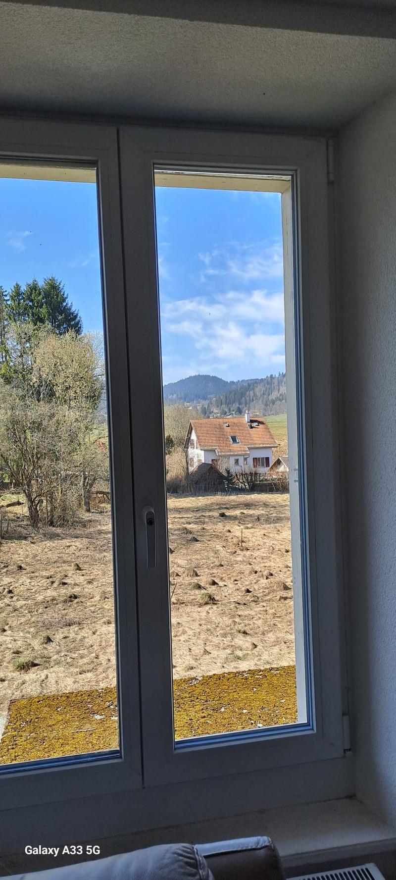 View from a window, showing a house in the distance, surrounded by trees and a field