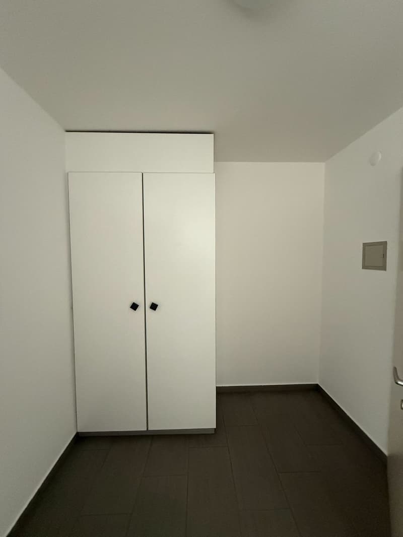 An empty room with white walls, a double door wardrobe, and wooden floor