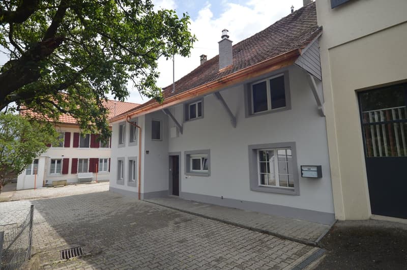 2 story white house, brown roof, brick driveway, trees in front, mailbox on wall