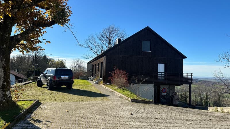 Single story house, black exterior, green lawn, brick driveway, balcony, elevated, SUV parked