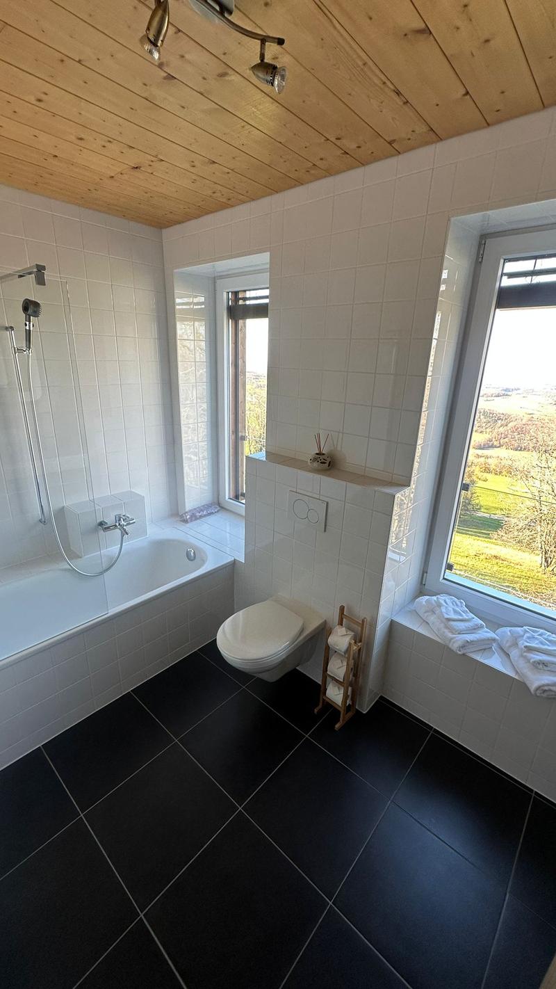 Bathroom with bathtub, toilet, windows, and white tiled walls and floor