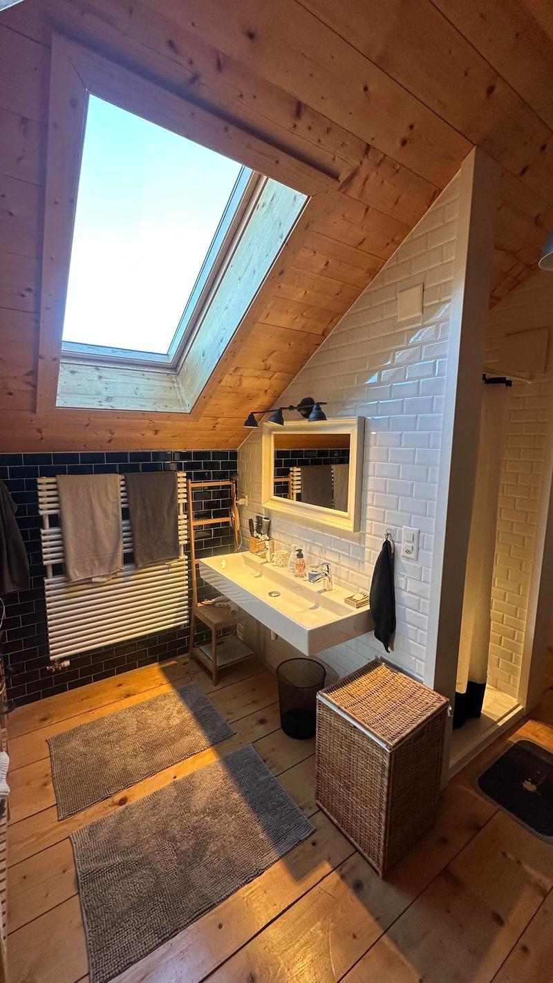 bathroom with shower, white wall, wooden floor, skylight, sink, mirror, towel racks, and rug