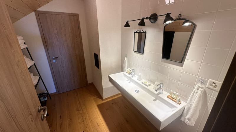 modern bathroom, wooden floor, white tile, double sink, mirrors, bathroom fixtures, shelves, door