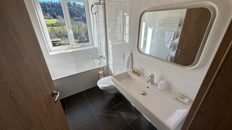 white bathtub, white tiles, white sink, glass shower with window, white mirror, toilet