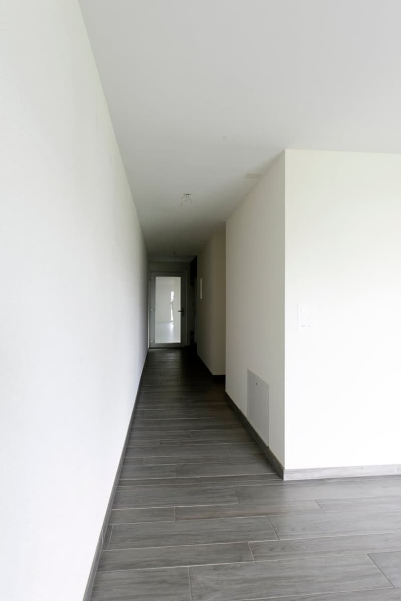 Empty hallway with white walls, gray tile flooring, and a door at the end.