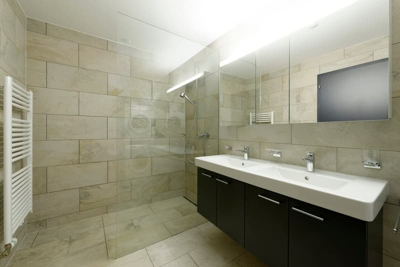 modern bathroom with double sink, glass shower enclosure, beige tiles, towel rack, mirror