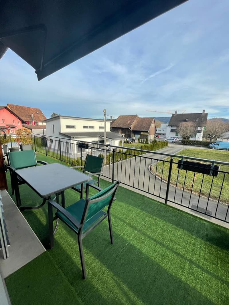Balcony with table and chairs, green artificial grass, metal railing, view of the surroundings