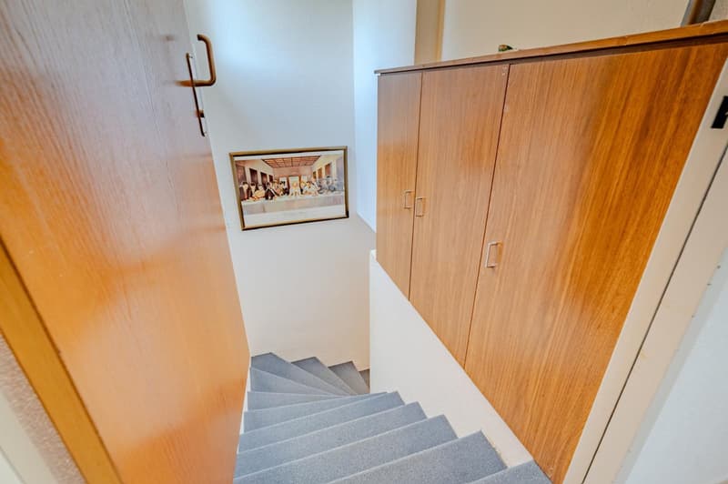 Wooden cabinets, framed artwork on the wall, and a staircase leading to the upper floor.
