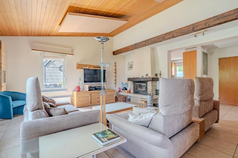 Spacious living room with wooden ceiling, large windows, gray sofas, coffee table, TV stand, and a fireplace