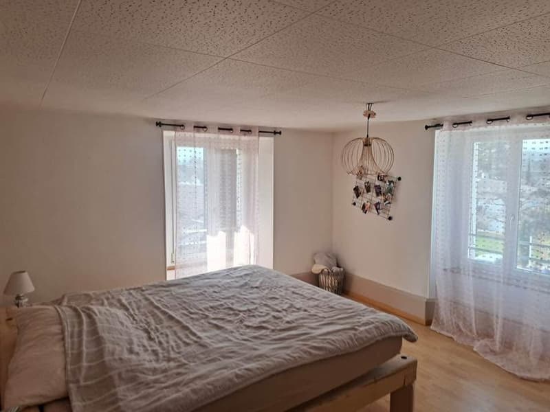 Bedroom with bed, lamp, windows with curtains, wooden floor, decorative items on wall