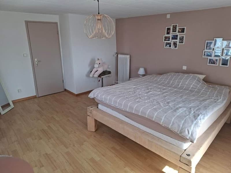 Bedroom with wooden floor, bed, lamp, stuffed toy, radiator, door, mirror, photo frames on the wall