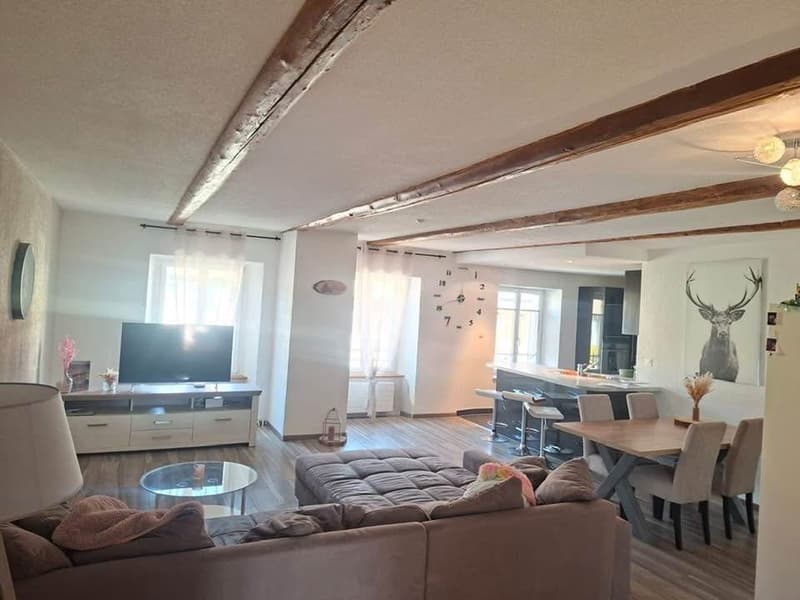 Living room with wooden floor, large sofa, dining table, TV, kitchen area, wooden beams on ceiling