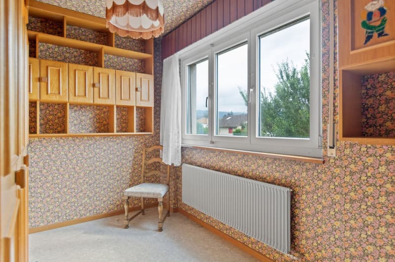 Cozy bedroom with floral wallpaper, wooden shelves and cabinets, large windows providing a scenic view of the outdoors