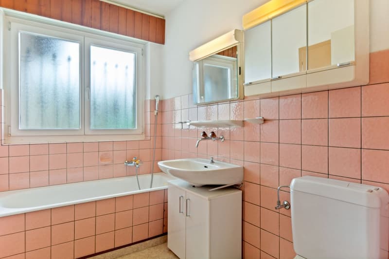 Bathroom with pink tile walls, bathtub, sink, and vanity cabinet with mirror above