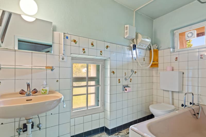 Bathroom with tiled walls, a sink, toilet, bathtub, mirror, and small window