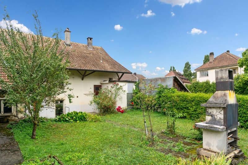 White and brown roof, chimneys, red flower plants, trees, bushes, metal firepit, grass