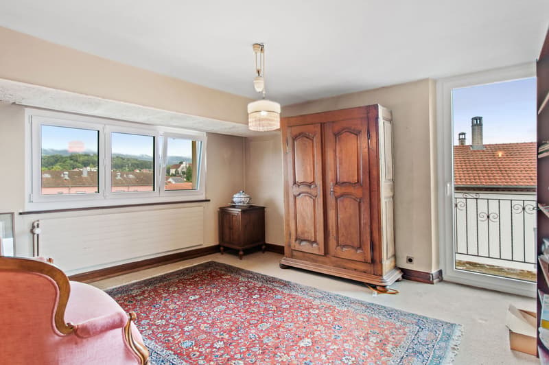 Spacious room with a balcony, wooden wardrobe, a large window, rug, chair, chandelier, small table with a bowl on top, and heater