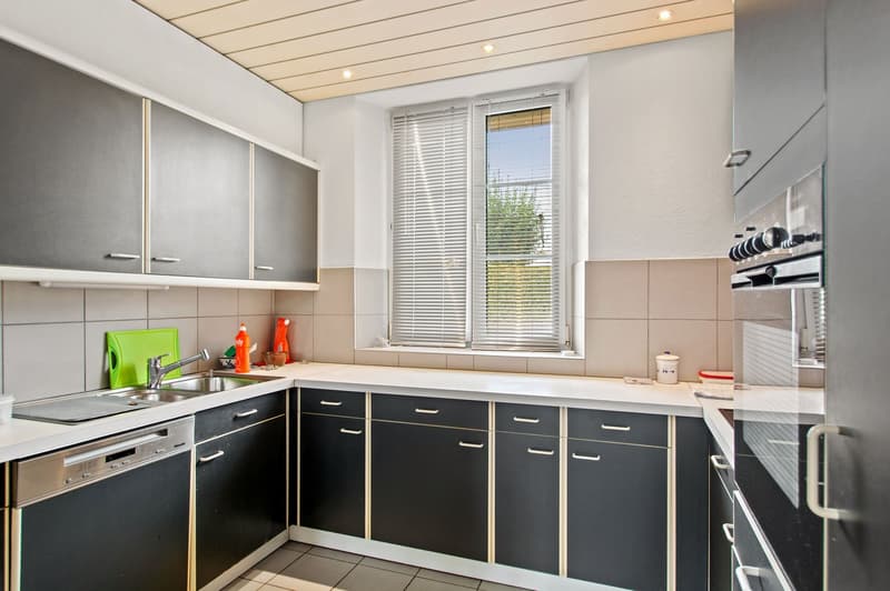 Modern kitchen with black cabinets, white countertops, dishwasher, and a stainless steel sink with faucet