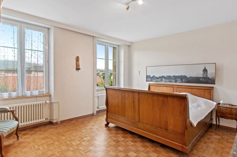 large wooden bed, wooden bedside table, radiators, wooden floors, two large windows, picture on wall