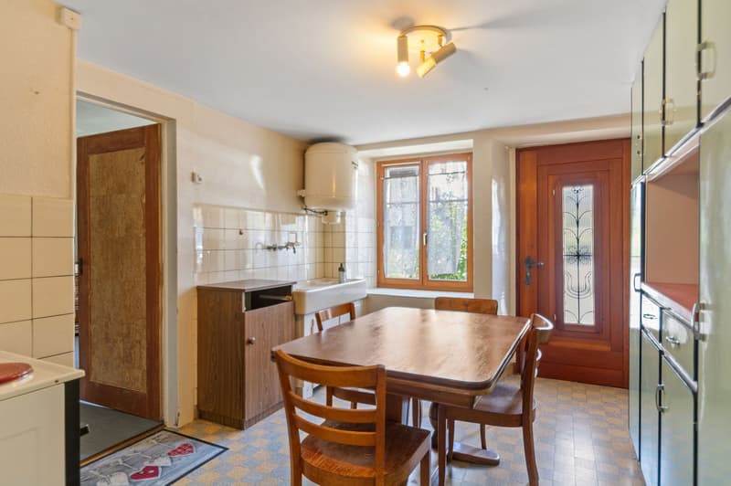 Wooden table, wooden chairs, white tiled wall, sink, cabinet, door, lamp