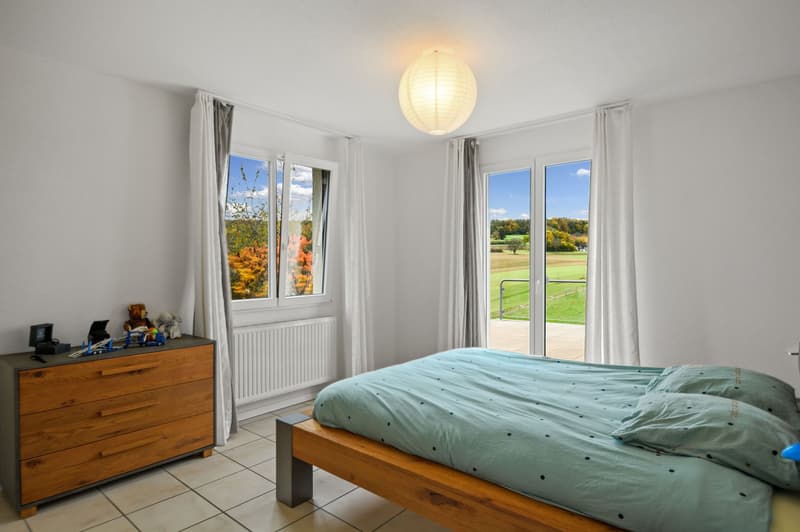 White walls, blue bedspread, wooden bed frame, wooden chest of drawers, large windows, sliding door, country landscape view