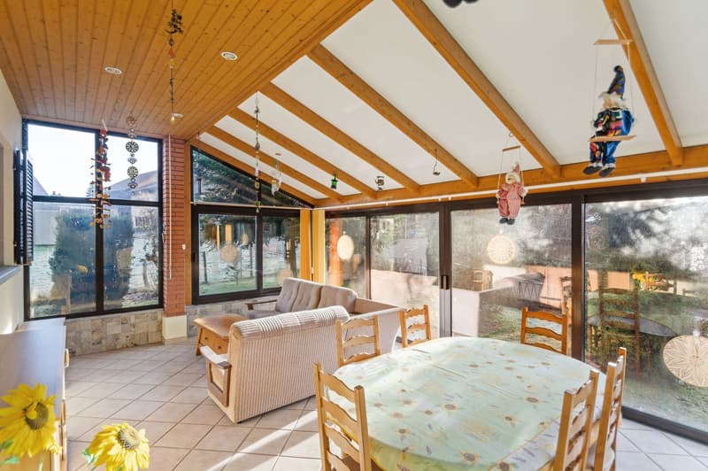 wooden ceiling, double-height windows, dining table, couches, tiles, sunflower-printed table cloth, decorations, hanging toys