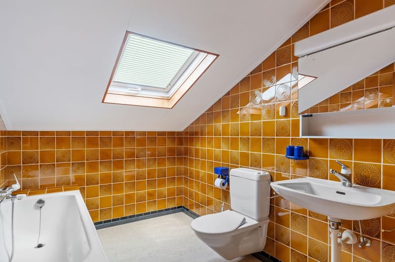 Bathroom with yellow tiles, bathtub, toilet, sink, skylight