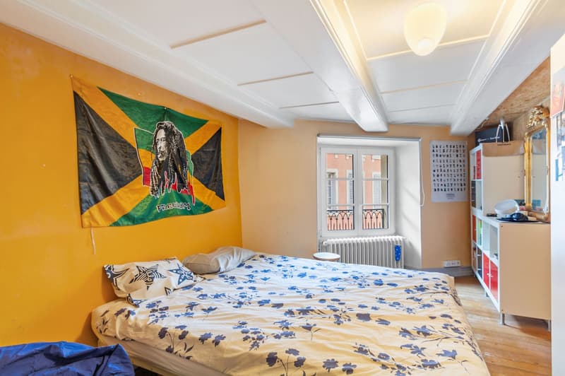 double bed, yellow walls, window with balcony, flag, shelves, radiator