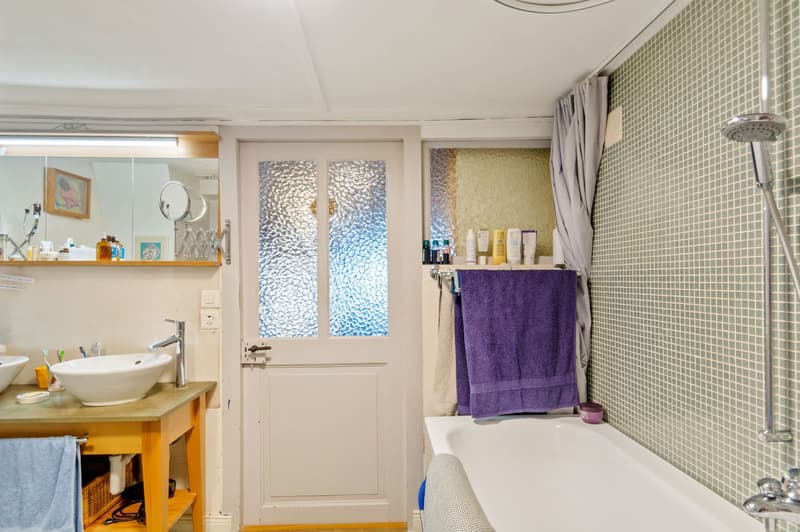 white bathroom with tiled walls, bathtub, sink, mirror, shower head, white doors, light blue towels, and white basin