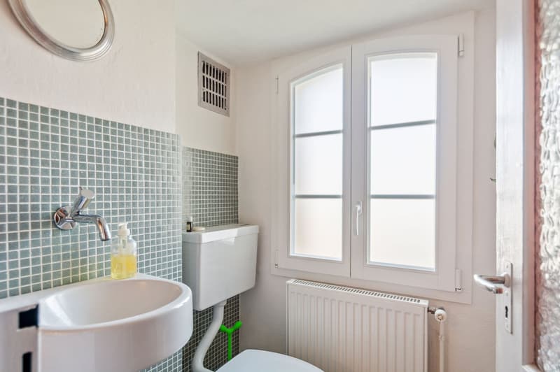 Bathroom, white sink, tiled walls, round mirror, toilet, faucet, small window