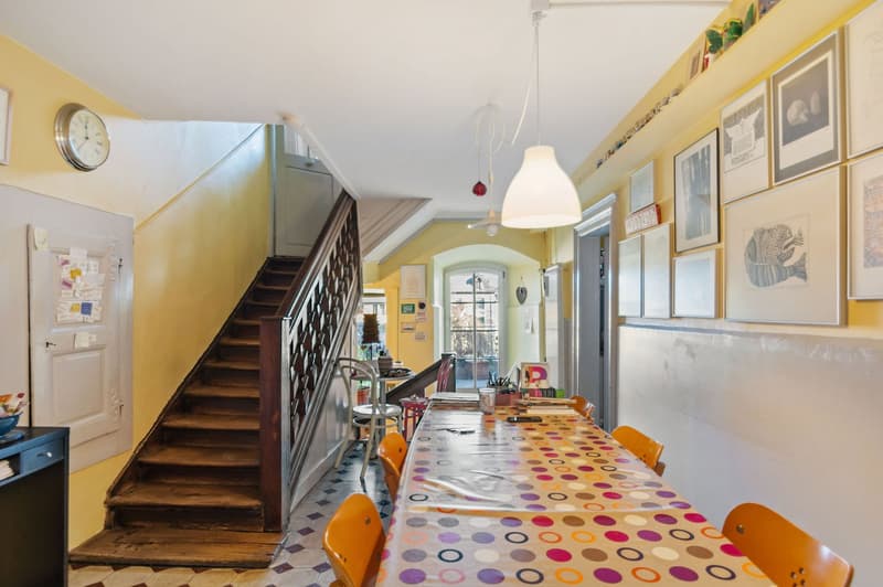 Dining room with a long colorfully dotted table, wooden chairs, decorative clock, and pictures on the wall