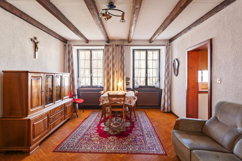 dining room with wooden dining table, chairs, wooden cabinet, rug, wooden beams, windows, cross on wall, mirror, couch