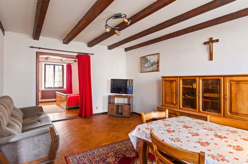living room with couch, TV, dining table, wooden cabinet, wooden floor, wooden beams, cross on wall