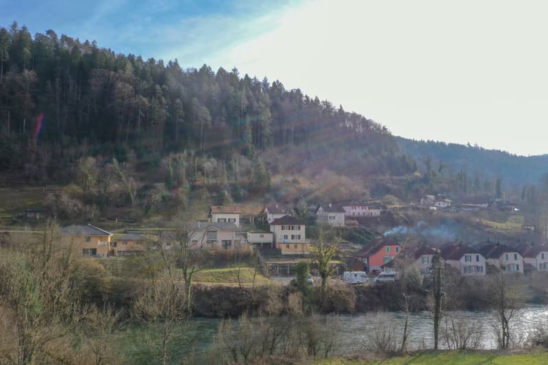 Houses on a hillside overlooking a river, surrounded by trees and mountains