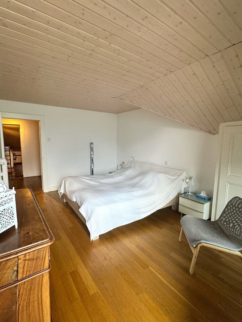 a raised ground floor bedroom with a large double bed, white sheets, a wooden desk, and a gray armchair