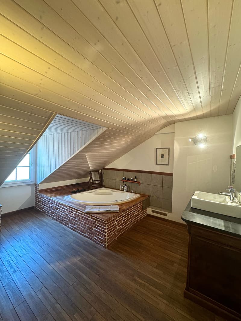 Bathroom with tub in attic, brick wall, wooden floor, white ceiling, mirror, sink, picture frame