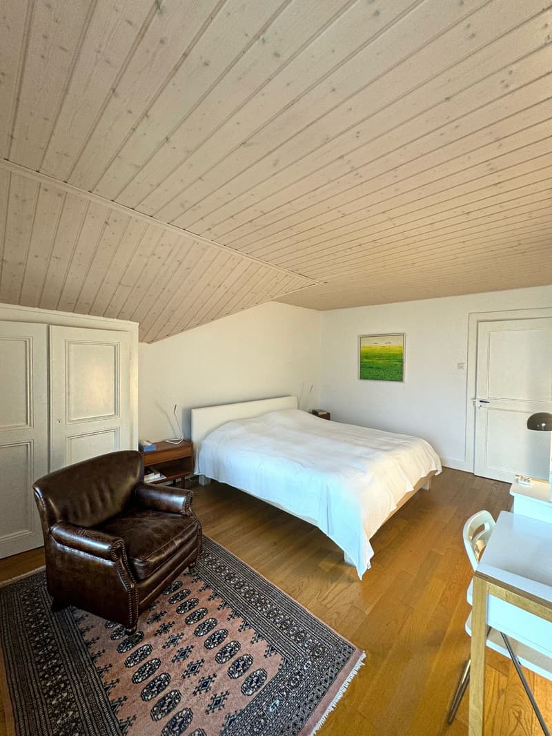bedroom with bed, nightstands, leather armchair, wooden rug, desk, picture on wall