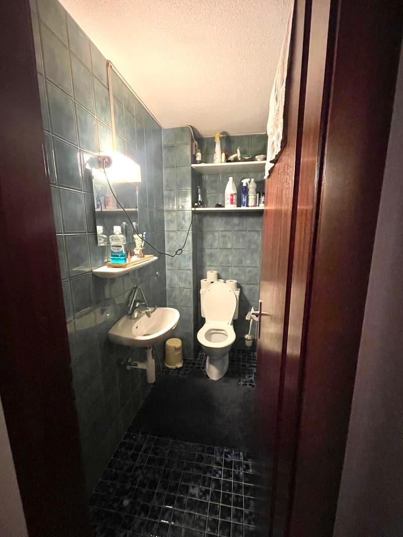 Small toilet room with sink and shelves, tile floor