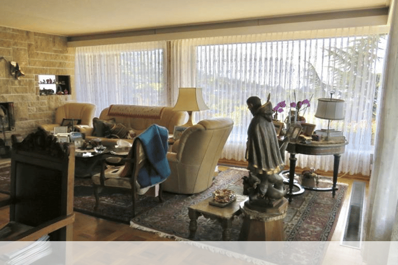 large windows, beige sofa, beige chairs, fireplace, wooden floor, table, statue, lamps, rug