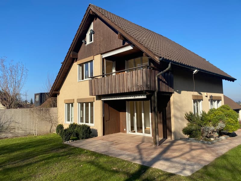 2-story house, beige walls, brown roof, brown balcony, sliding doors, patio, driveway, lawn, shrubs, plants