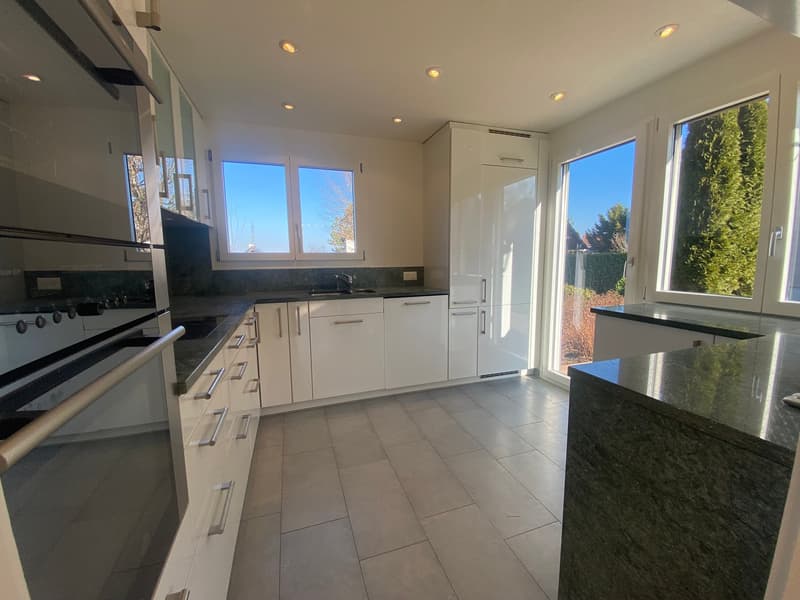 Modern kitchen with white cabinets, tiled floor, double stainless steel oven, granite countertops, sink with faucet, large windows.