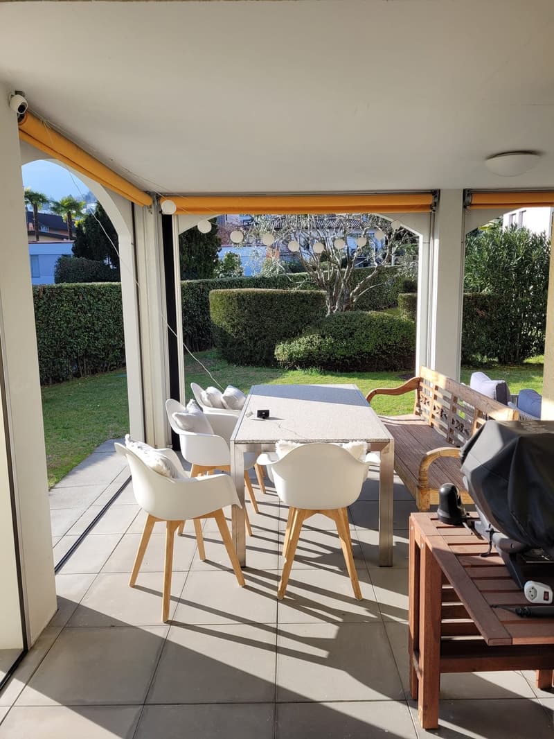 covered terrace with table and chairs, wooden bench, outdoor lighting, view of garden