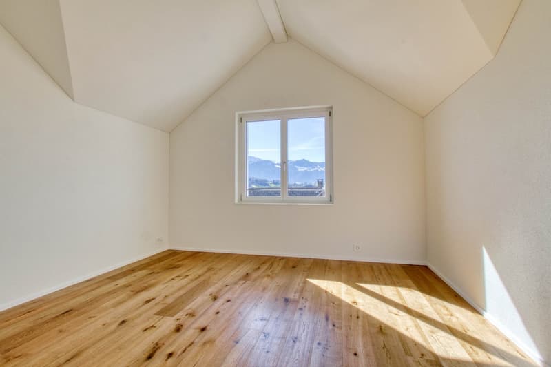 empty room, wooden floor, large window, slanted ceiling, mountain view
