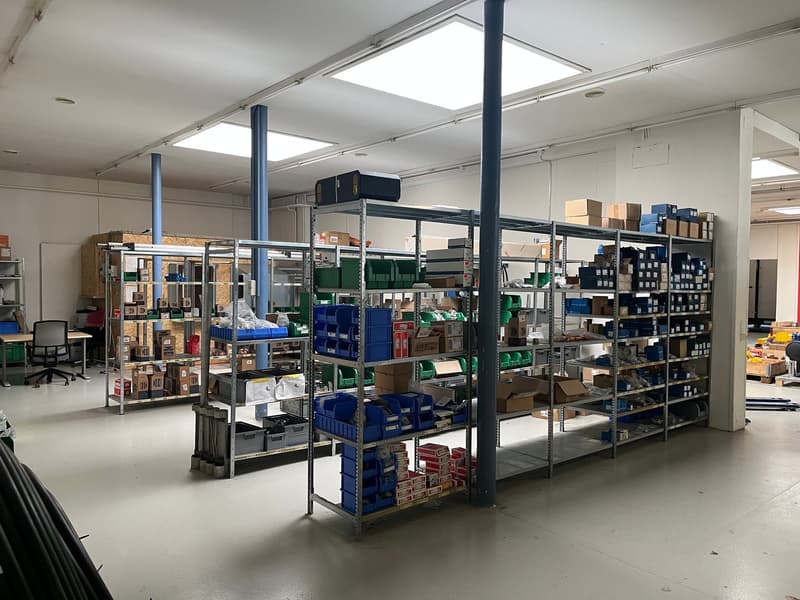 The image shows a large warehouse or storage facility with multiple rows of metal shelving units filled with various boxes, containers, and other supplies. The space is well-lit with overhead lighting and has a clean, organized appearance.