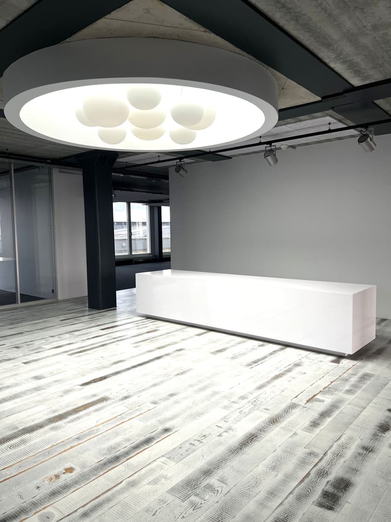 Large circular modern light fixture, large rectangular white reception desk, long room, white hardwood floors