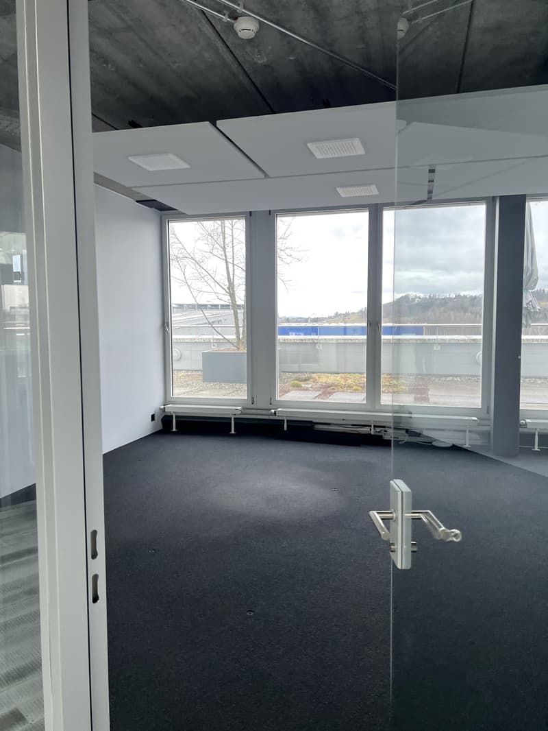 Large office space with wide windows and black carpet, visible exterior view